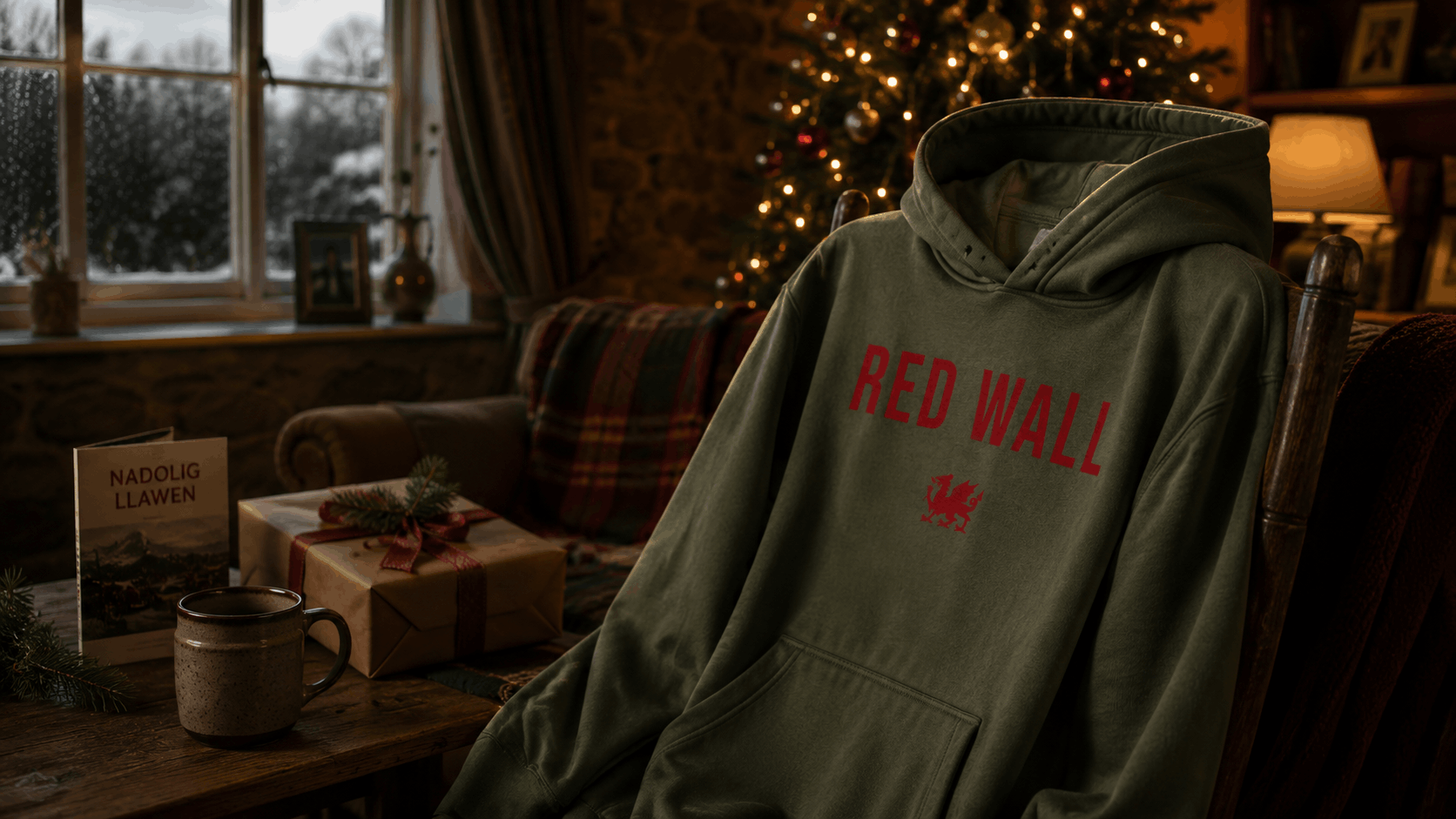 Red Wall Welsh hoodie by Made in Cymru displayed in a cosy Welsh Christmas setting with festive gifts and winter atmosphere.