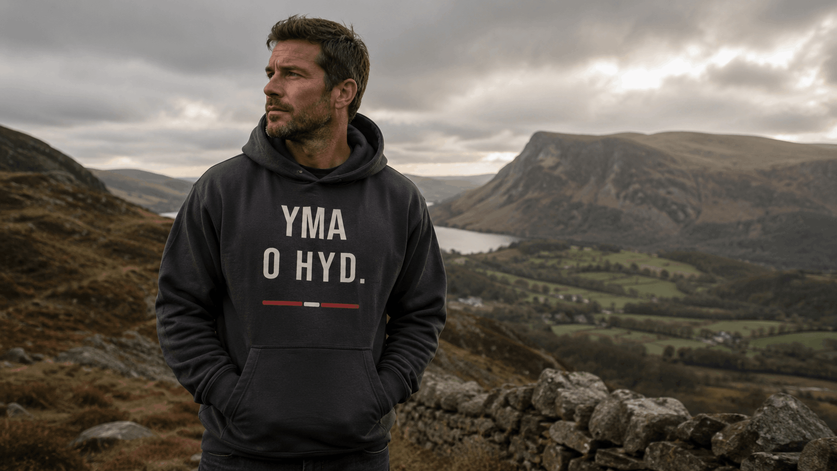 Welsh man wearing the Yma O Hyd hoodie on a North Wales hillside, representing Welsh identity, heritage and meaningful Welsh gifts for men.