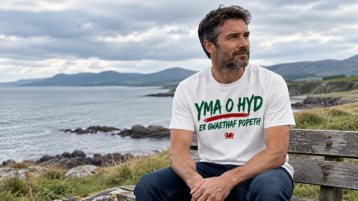 Man wearing white Yma O Hyd Er Gwaethaf Popeth Welsh T-shirt with red dragon below the lettering on the North Wales coast