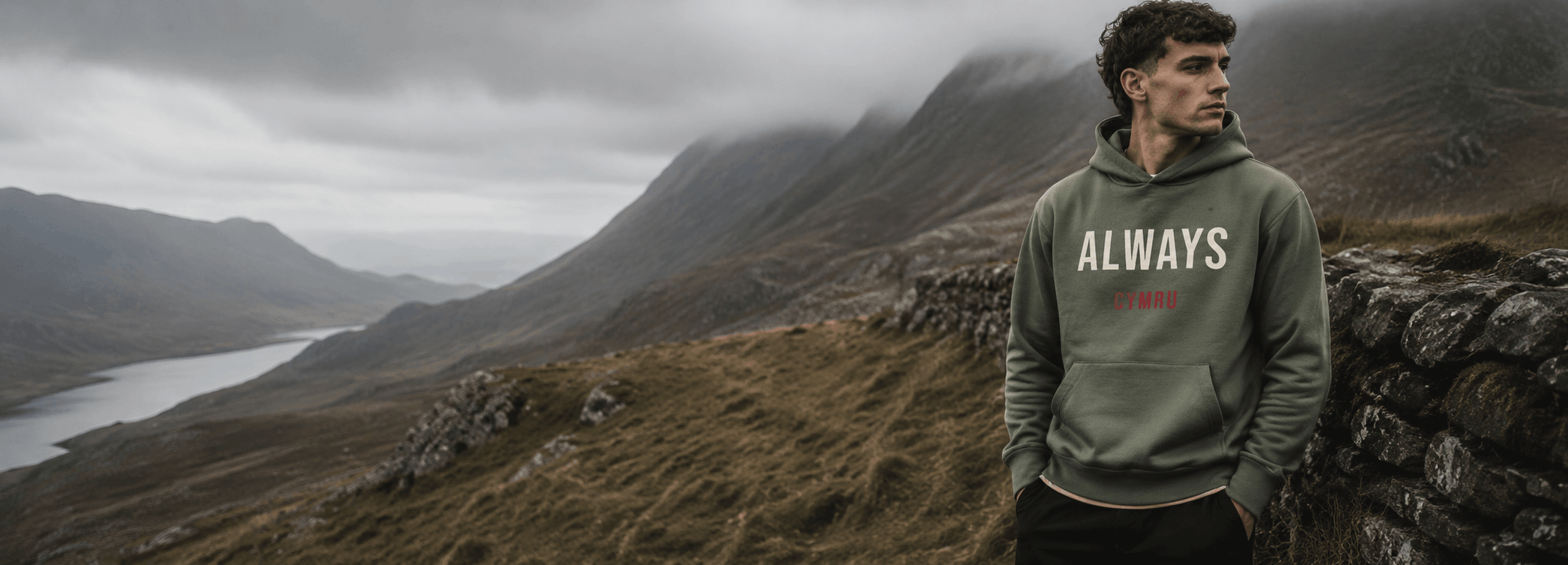 Man wearing a hoodie with 'ALWAYS' text standing on a mountainous landscape.