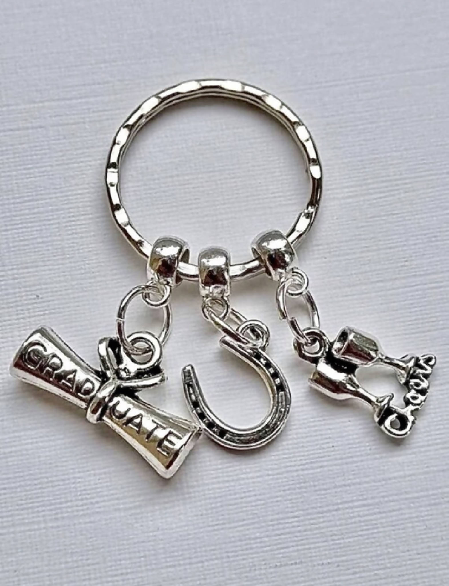 Graduation gift keyring with 3 charms; a scroll, a lucky horseshoe and two goblets, and the word ‘Cheers’. A super gift for a graduate.