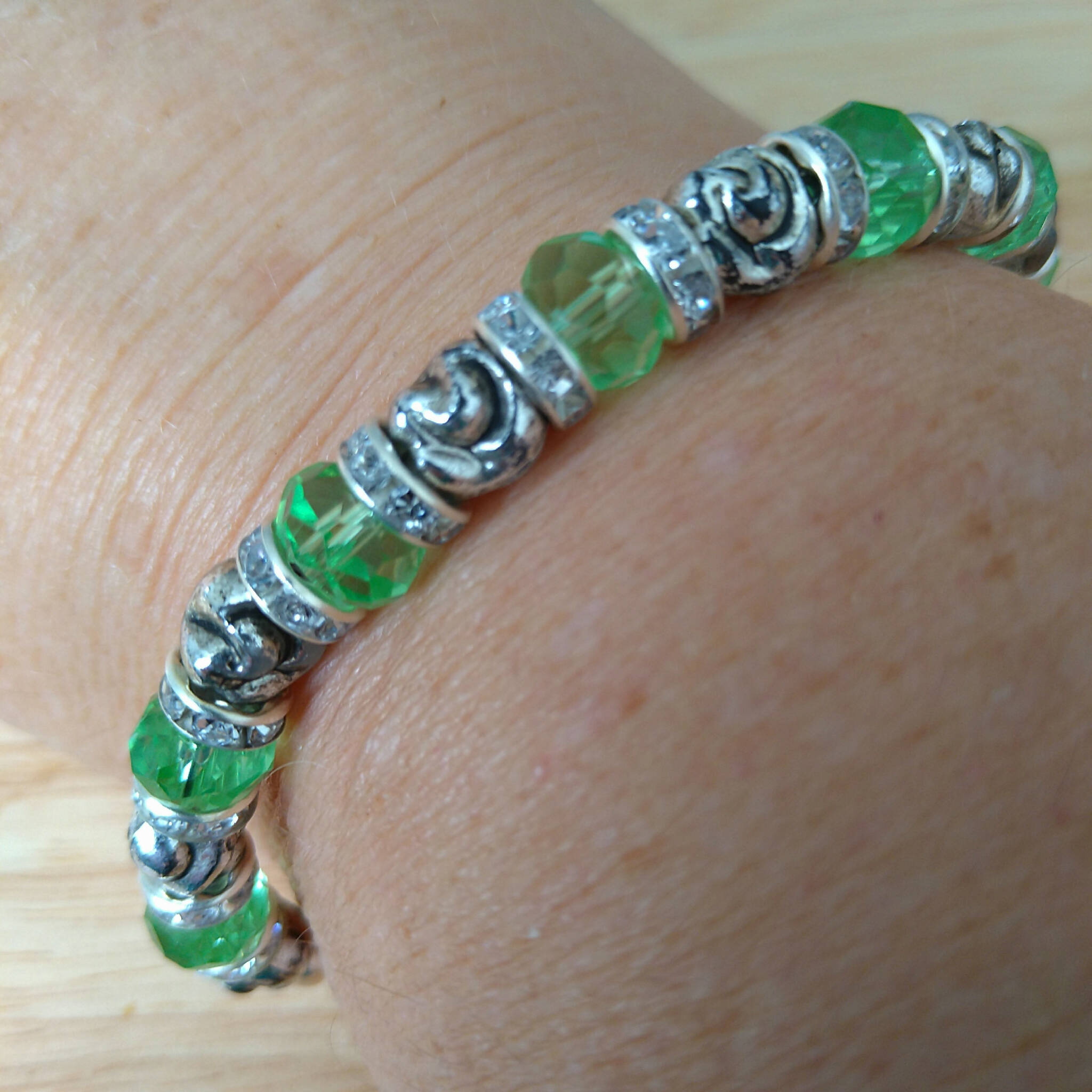 Handmade bracelet with recycled green & silver coloured beads & rhinestone rondelle spacers. On wrist. Upcycled.